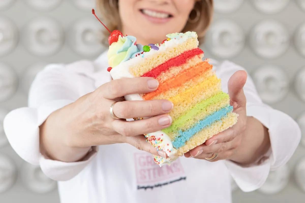 Grace holds out a slice of rainbow cake