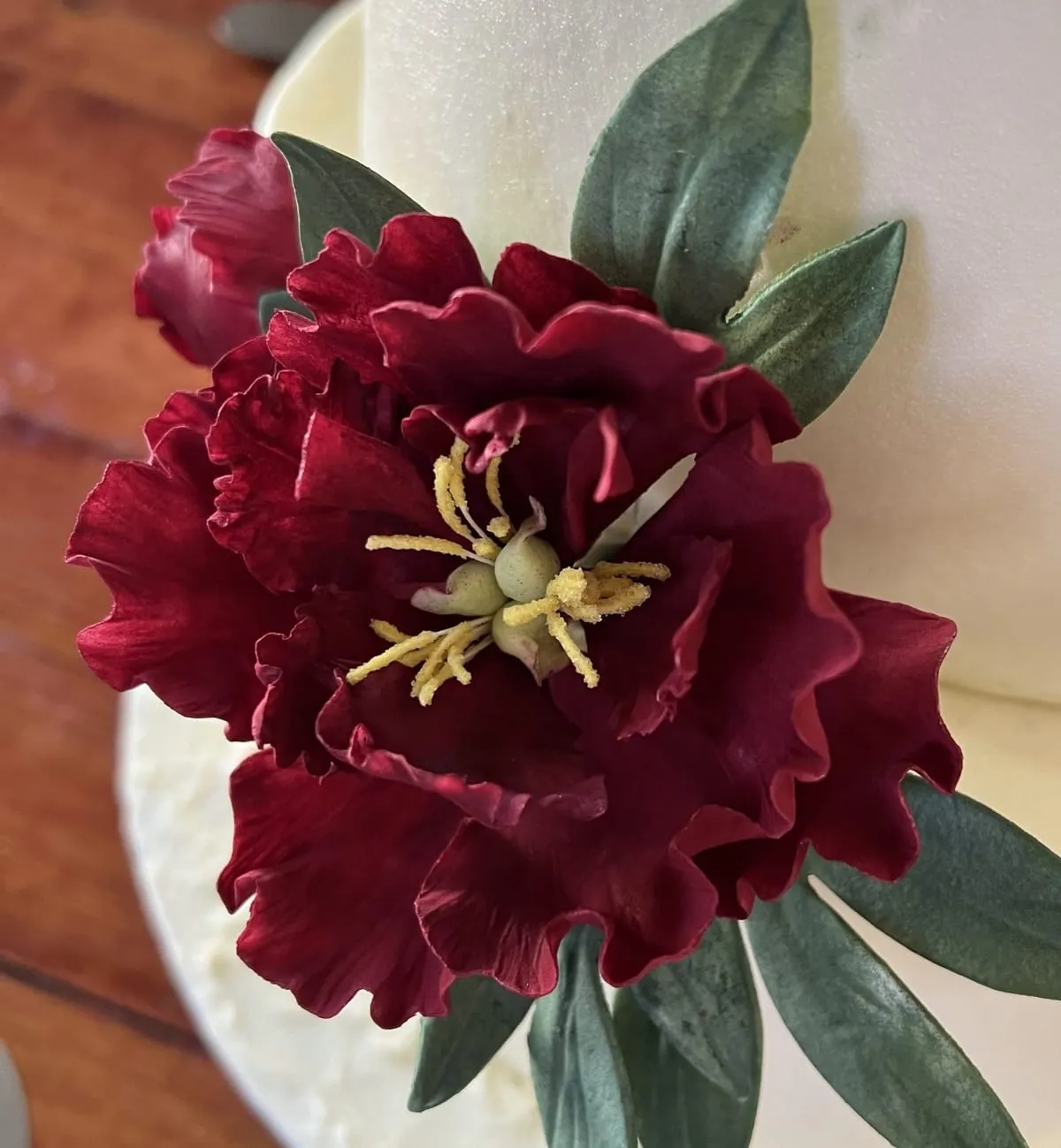 A dark red sugar peony on a white cake