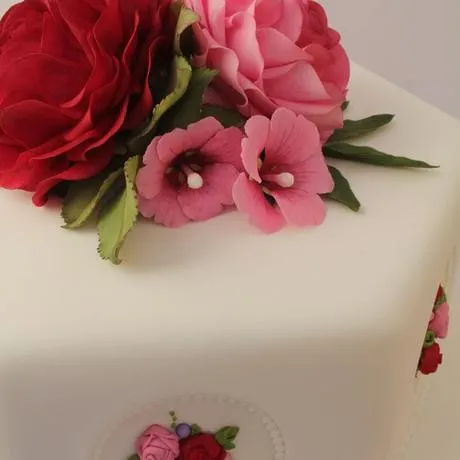 A white hexagonal cake with red and pink sugar roses and hollyhocks