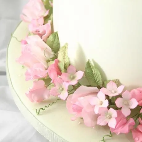 A white wedding cake with a ring of pink sugar sweet peas